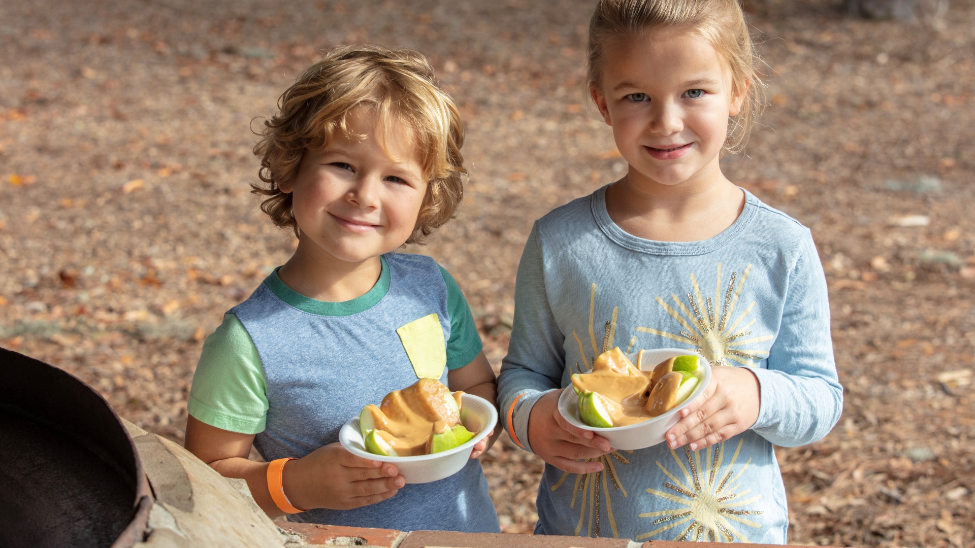 Two children holding bowls full of apples smothered in caramel sauce