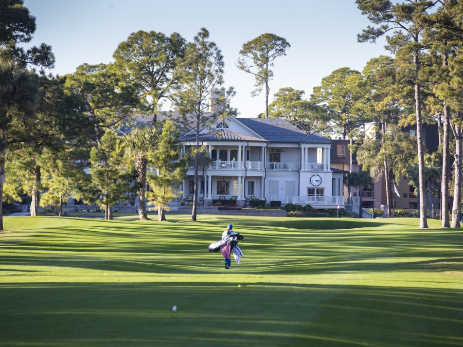 One golfer walking the course with the inn in the background  