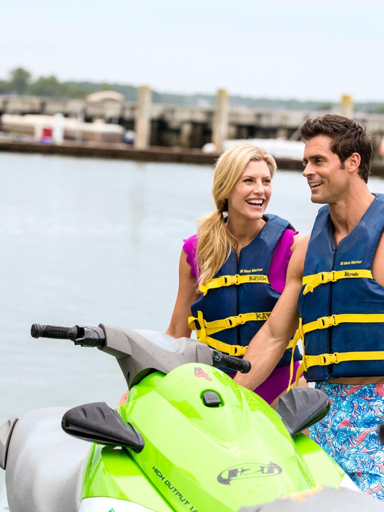 Couple laughing and standing next to a jet-ski 